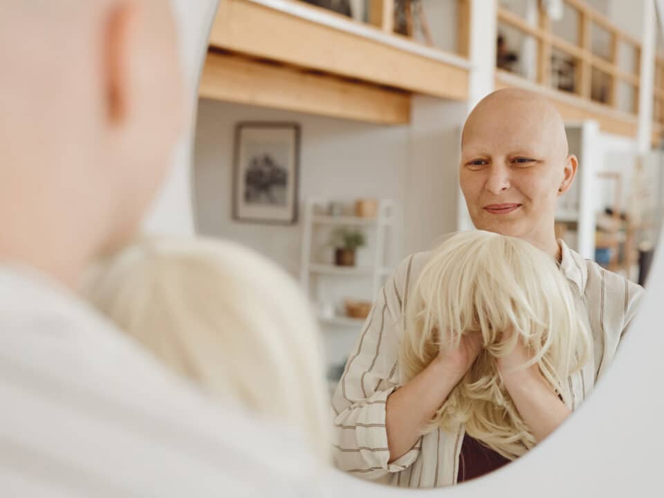 Bald Cancer Patient Smiling While Holding a Wig in Front of the Mirror