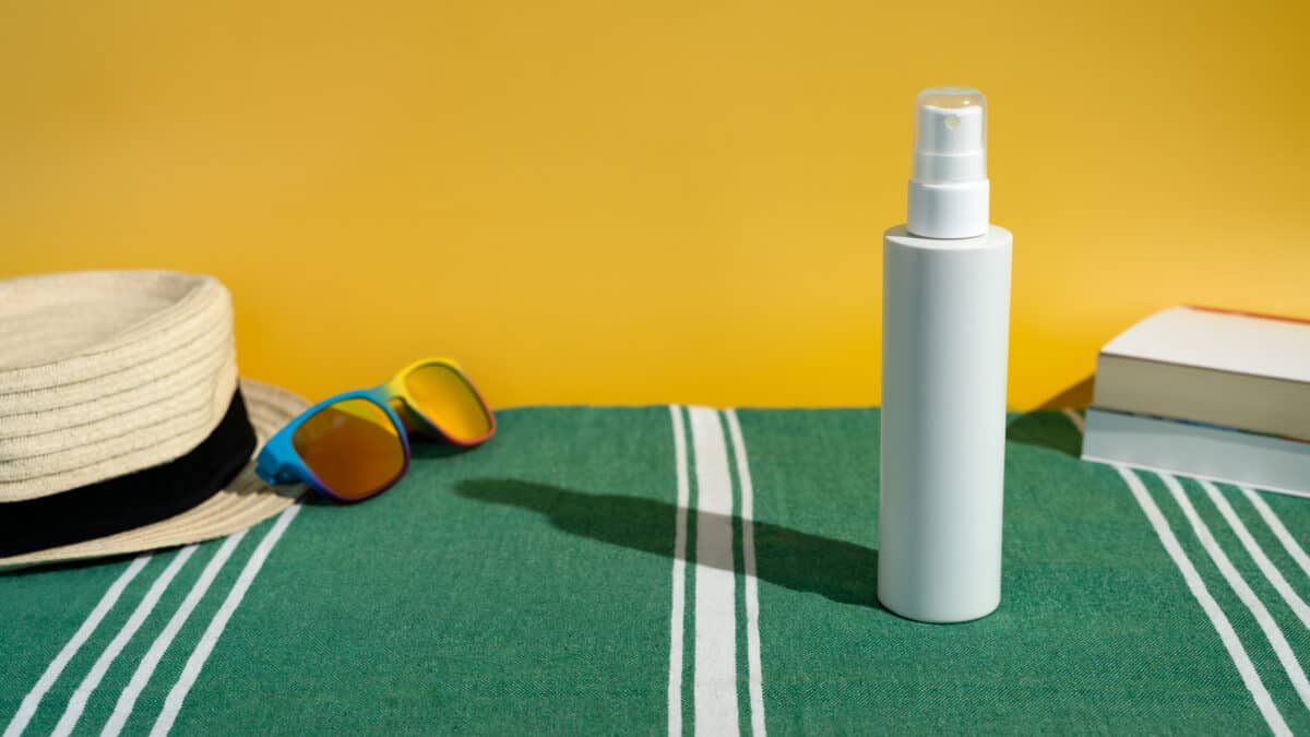 Blank sunscreen bottle sun hat and sunglasses books on beach towel