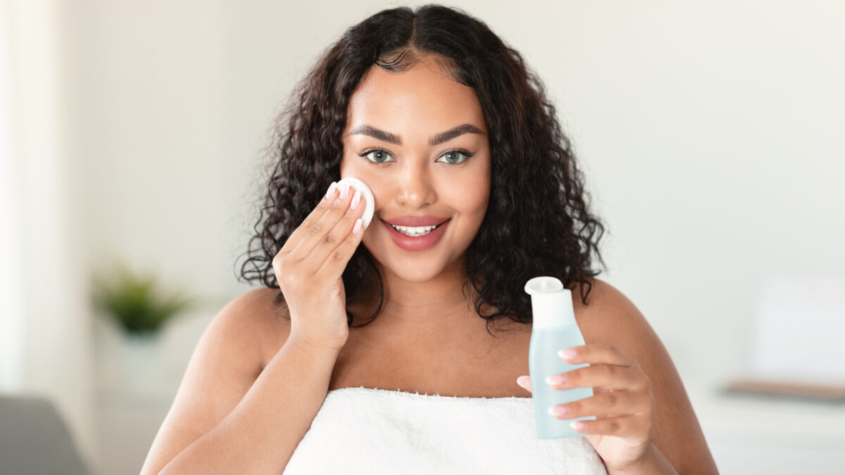 Beautiful black body positive lady cleaning her face from makeup with cotton pads and micellar water, home interior