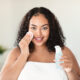Beautiful black body positive lady cleaning her face from makeup with cotton pads and micellar water, home interior