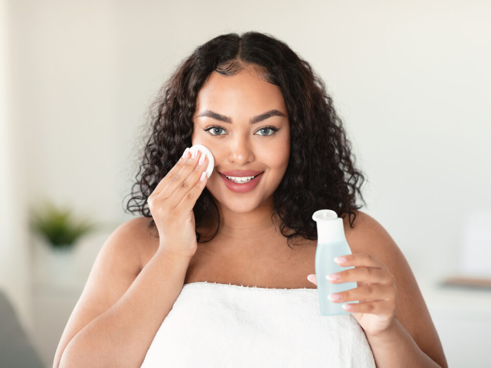 Beautiful black body positive lady cleaning her face from makeup with cotton pads and micellar water, home interior